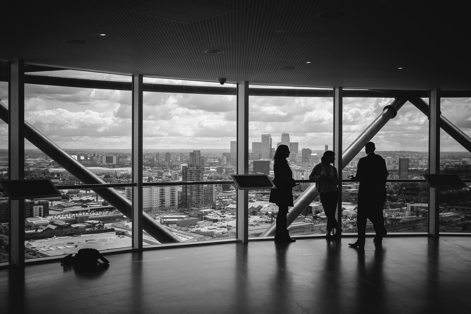: Black-and-white photo of professionals standing together in a tall office building with floor-to-ceiling windows overlooking a city skyline, symbolizing teamwork, growth, and embracing new perspectives in sales culture.